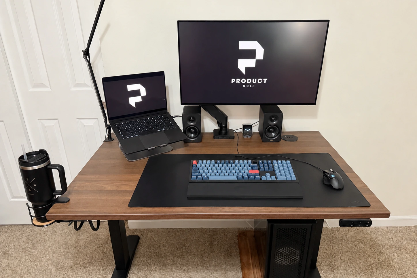 The UPLIFT V3 standing desk set up with a laptop stand, Dell monitor, speakers, keyboard, mouse, and cup holder