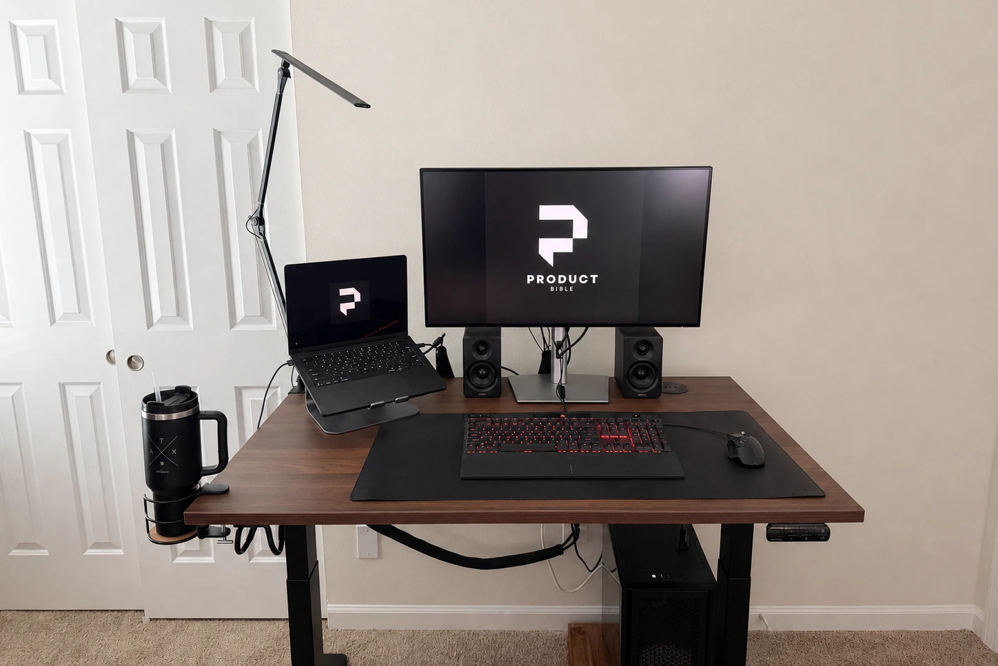 The UPLIFT V3 standing desk set up with a laptop stand, Dell monitor, speakers, keyboard, mouse, and cup holder